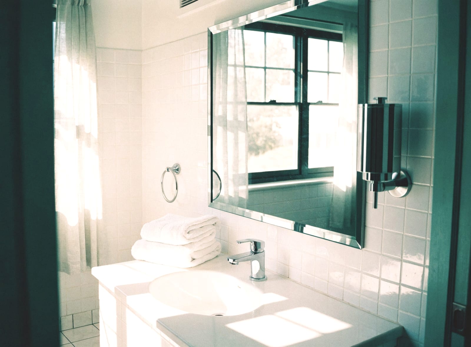 Bathroom with green tiles, a mirror and a stack of folded white towels